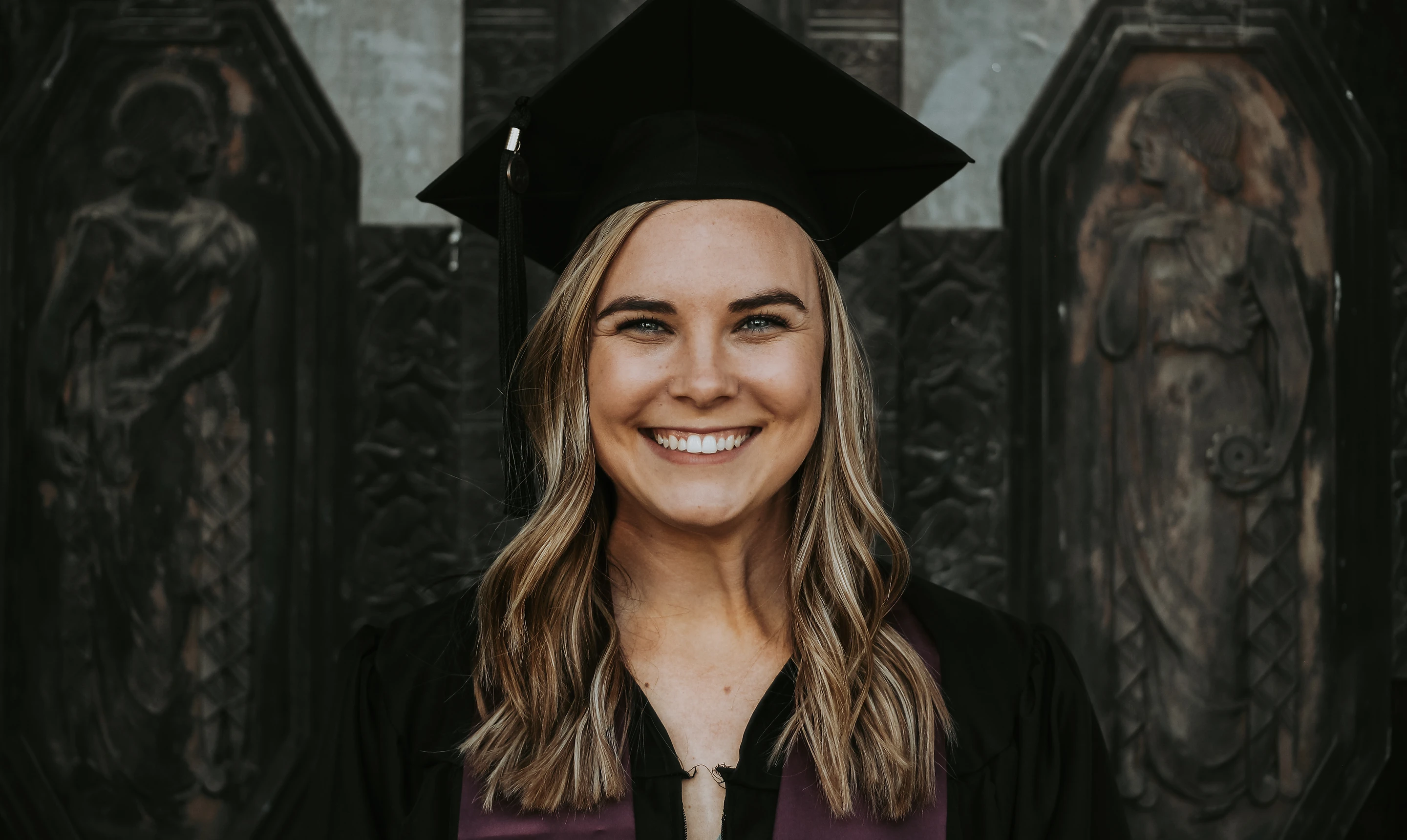 Young woman in graduation cap smiling in front of doors.