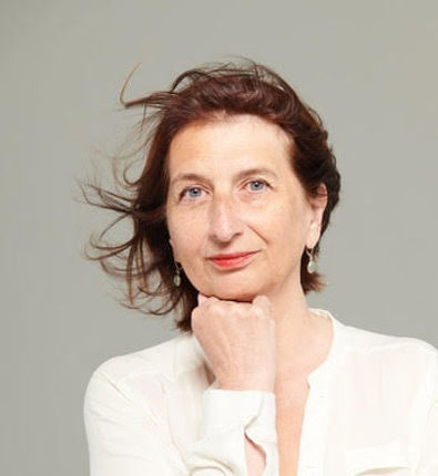Image de Jeanne Thiriet, une entrepreneure de 50 ans et plus. Elle pose son menton sur sa main, porte une chemise blanche et a les cheveux qui flottent au vent.