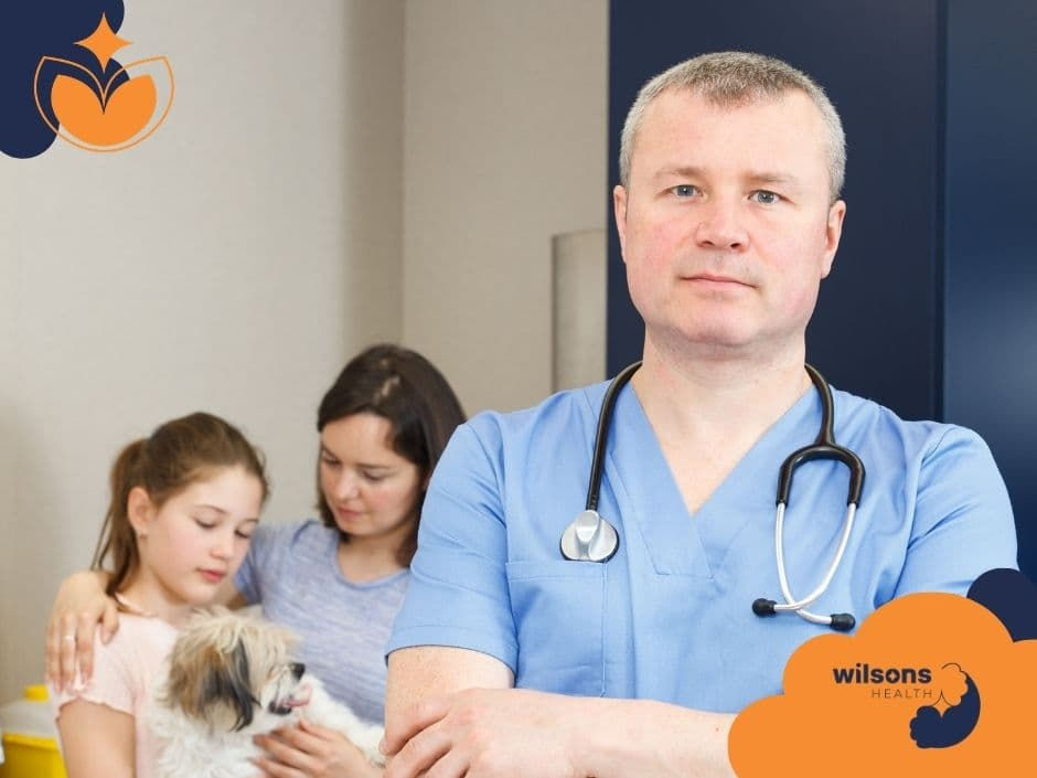 A doctor in blue scrubs with a stethoscope stands confidently. A woman and girl with a dog are in the background. Wilsons Health logo visible.