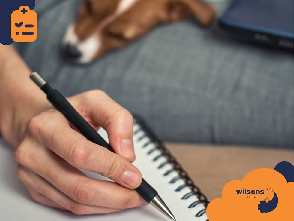 Hand writing with a pen on a notebook, a dog sleeping in the background. Logos: clipboard icon and "Wilsons Health" in orange and blue.