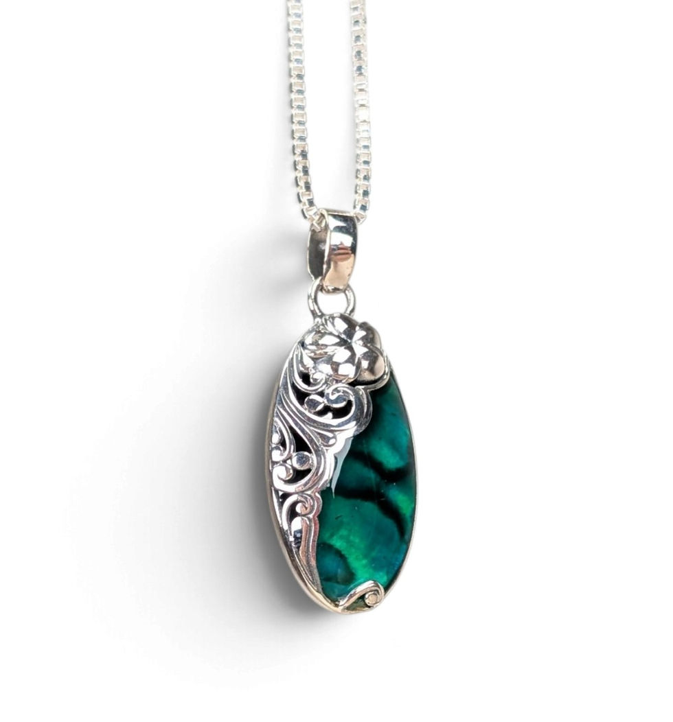 Ornate silver-toned pendant with an elongated faceted emerald-green gemstone