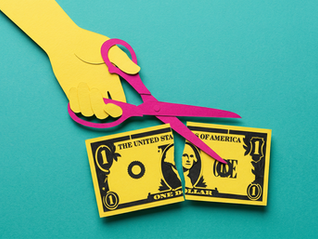 Yellow paper hand with pink scissors cuts a yellow dollar bill on a turquoise background, conveying themes of financial decisions.