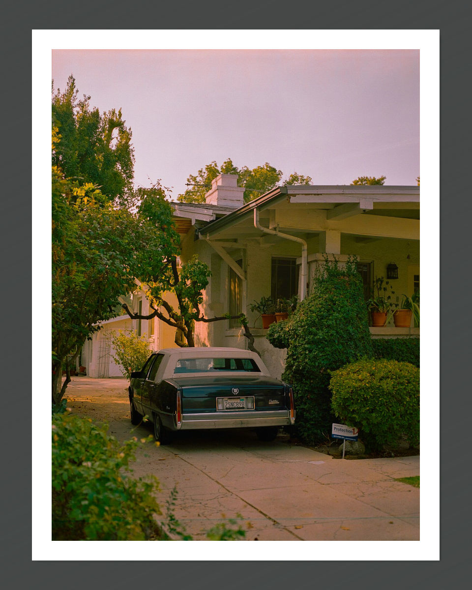 A fine art print featuring a classic car parked in front of a house with a warm-toned sunset in the background.