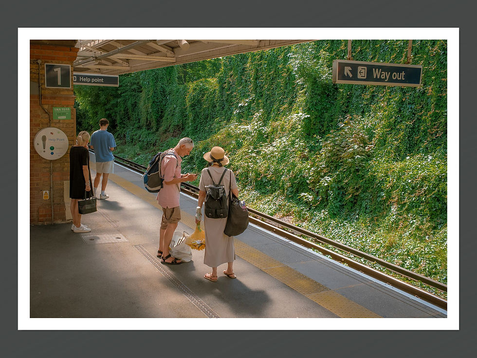 An image featuring a train station platform with two people standing on the platform, surrounded by greenery and train tracks