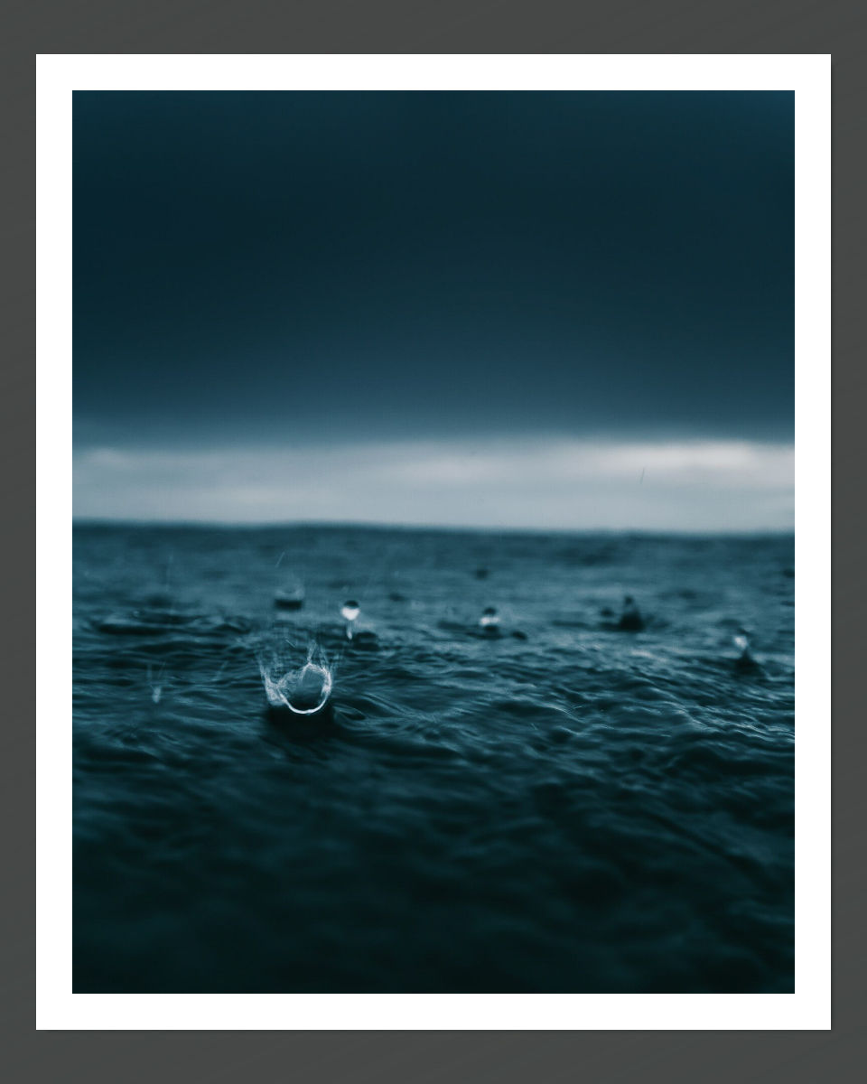 An image of raindrops hitting the surface of a waterbody with an artistic blue tint