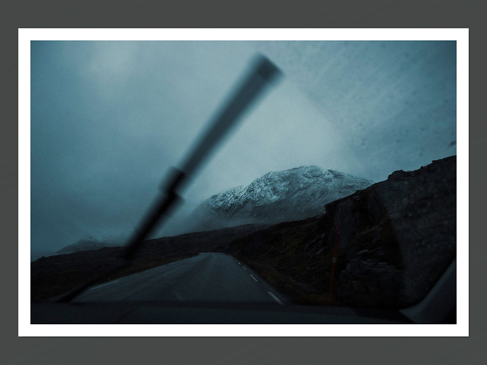An image of a snow capped mountain taken from within a car on the road with a visible windshield wiper in view