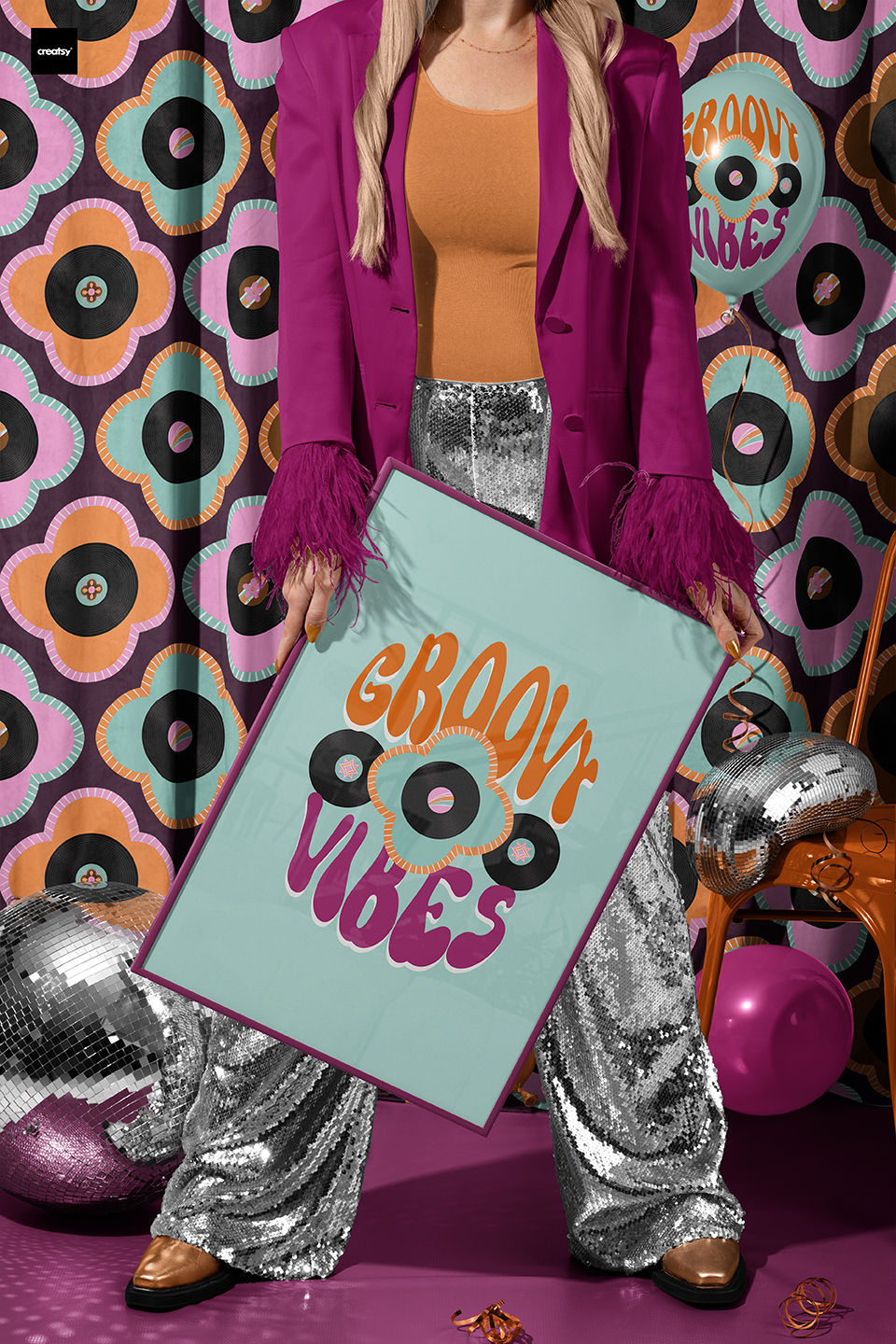 Lady wearing a magenta coat and silver disco pants holing a Groovy Vibes 70s art print in front of a retro turquoise, pink and orange curtain with vinyl records and quatrefoils flowers