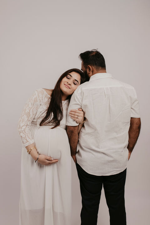 Expectant couple embracing for maternity shoot in indoor studio setting.