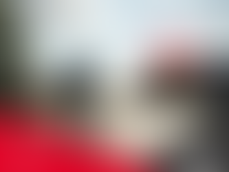 Pessoa andando de bicicleta em rua vazia e ao fundo estabelecimento com painel de led escrito "2026" - na parte de baixo, elementos gráficos nas cores cinza escuro e vermelho com escritas "Feliz Ano Novo!" e logo da empresa Bicicletas Monark SA em branco