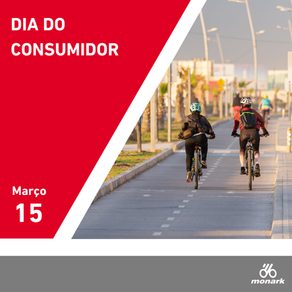 Ciclistas em uma pista ao ar livre, cercados por postes e vegetação. Texto: Dia do Consumidor, 15 de março. Logo da Bicicletas Monark SA.