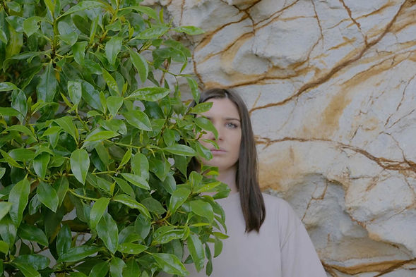 A woman stands against a rock wall hidden by greenery