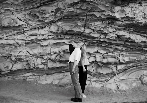 Strange Nature - two women stand back to back against a rock wall