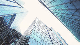 Looking up at glass skyscrapers with a modern design against a bright sky. Blue-tinted reflections create a sleek, urban atmosphere.