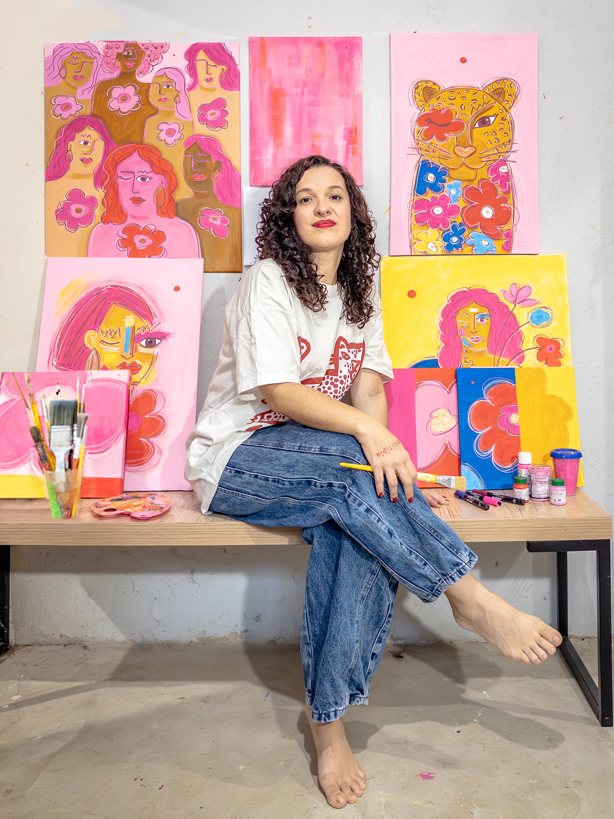 Elisa em seu ateliê, cercada de pinturas coloridas