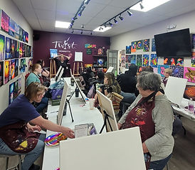 People painting on canvases on a table.