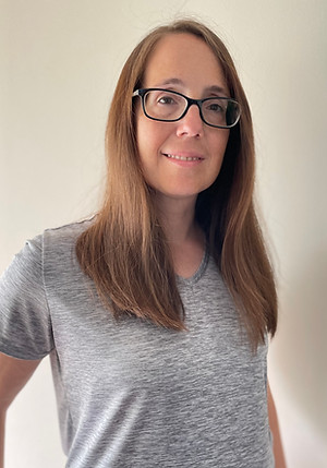 MiaMaria a woman in a grey shirt with medium brown hair  and glasses smiling