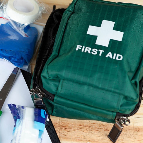 Selection of first aid equipment including scissors, bandages, gloves, and dressings beside a green first aid bag.