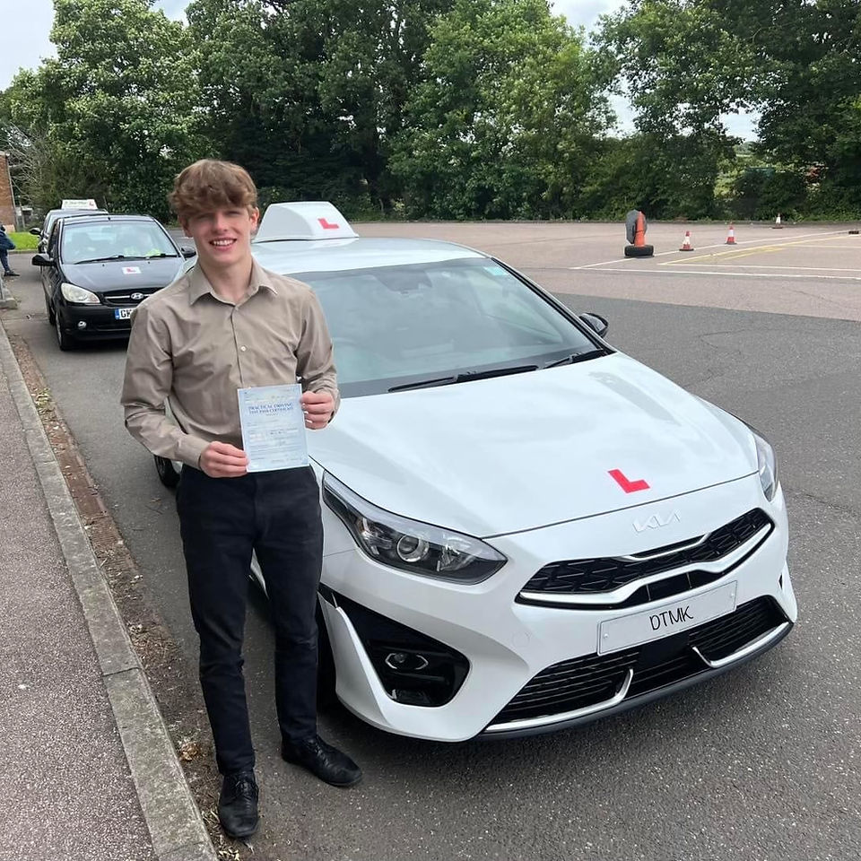 Newly qualified driver holding a driving test pass certificate beside a white learner car with L plates after passing a UK driving test.