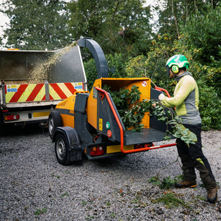 Tree surgeon operating wood chipper equipment during outdoor work, highlighting the importance of workplace first aid training.