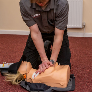 Trainer performing chest compressions on a CPR manikin with female chest anatomy to reflect inclusive first aid training.