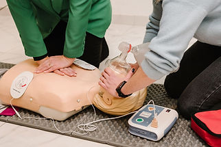 Learners practising CPR with rescue breaths on a resuscitation manikin using a bag-valve mask and AED trainer