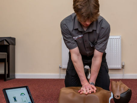 DTMK Training Services instructor performing chest compressions on a Laerdal QCPR CPR training manikin while a tablet displays real time compression feedback during a first aid training session in Milton Keynes.