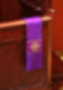 Purple stole with gold crosses draped over a dark wooden confessional, set against a red background. The mood is solemn and religious.