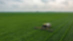 Aerial view of multiple farming machines harvesting a vast green field, showcasing large-scale agriculture.
