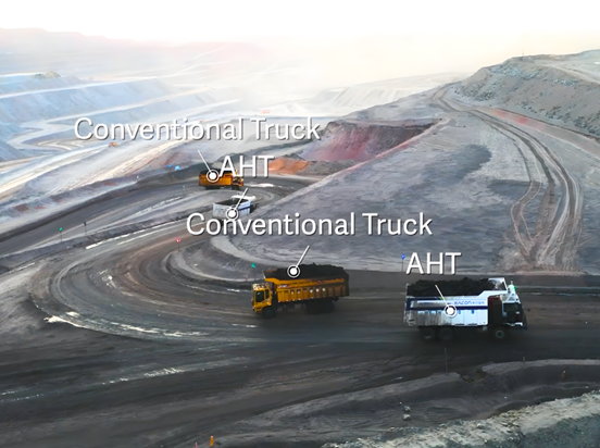 Mining site with two labeled trucks, "Conventional Truck" and "AHT," on a curving road. Earthy tones and expansive quarry backdrop.