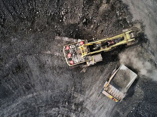 Aerial view of a yellow mining excavator loading a dump truck on dark rocky ground, with dust and an OpenAutonomy logo.