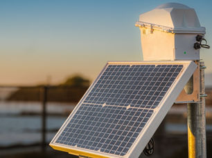 Solar-powered GNSS reference station mounted on a pole at sunset — the physical infrastructure behind RTK corrections delivery for autonomous fleet positioning