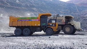 An autonomous wide body haul truck operating alongside a manually driven rigid-body truck on a shared haul road at an open-pit mine, illustrating mixed-fleet autonomous haulage in a brownfield production environment.