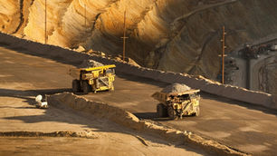 Two large autonomous haul trucks operating on tiered haul roads in a deep open-pit mine, surrounded by steep high walls that can obstruct GNSS satellite signals and cause positioning degradation.