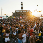 Multidão se divertindo no circuito Barra-Ondina ao pôr do sol no Carnaval de Salvador 2026, em frente ao Farol da Barra..