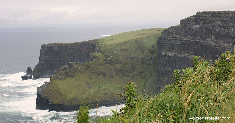 Steil abfallende Küste in Irland, grün bewachsen, sehr dunkle Felsen, wildes Meer - Blog zu Buchrezension von Nuala O'Faolain Blog Wortfeger Atelier