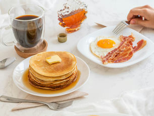 Diner breakfast of pancakes, a fried egg and bacon, with a cup of black coffee.