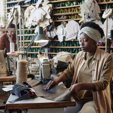 Two women work with leather while sitting at the sewing machines of a small shoe shop.