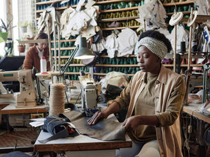 Two women work with leather while sitting at the sewing machines of a small shoe shop.