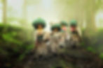 Women in traditional attire carry large sacks through a misty forest path. The scene is lush green, creating a serene and hardworking mood.