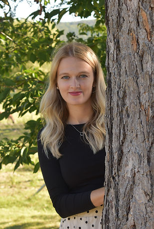 Fotografie učitelky I. třídy školy, učitelka vykukuje za stromem.