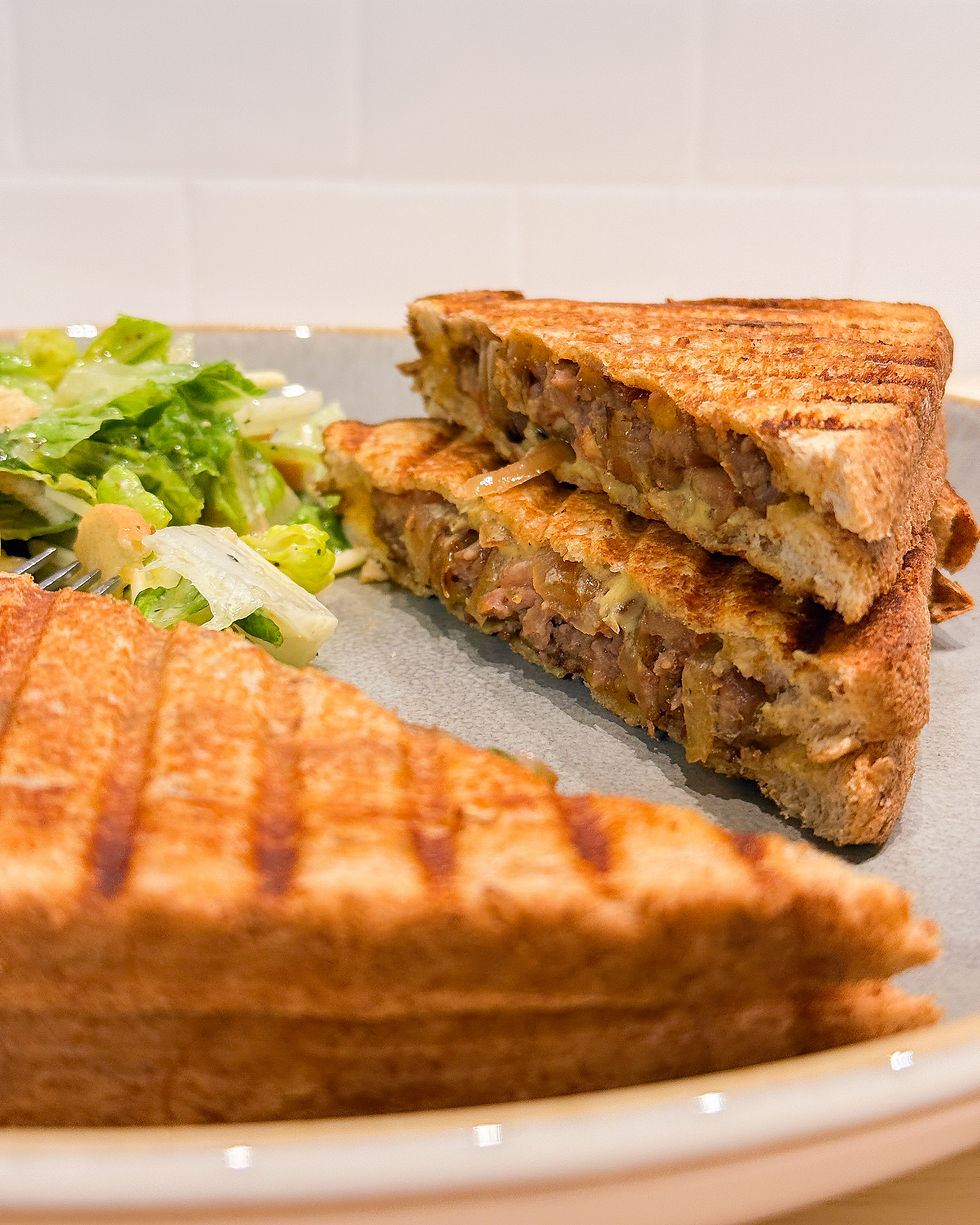 Toasted sandwich with melted cheese and meat filling on a plate, accompanied by a fresh green salad. Warm, inviting kitchen setting.