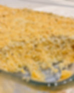 Golden breadcrumb-topped mashed potato casserole with a portion scooped out, revealing a creamy interior. Served in a clear glass dish on a tabletop.