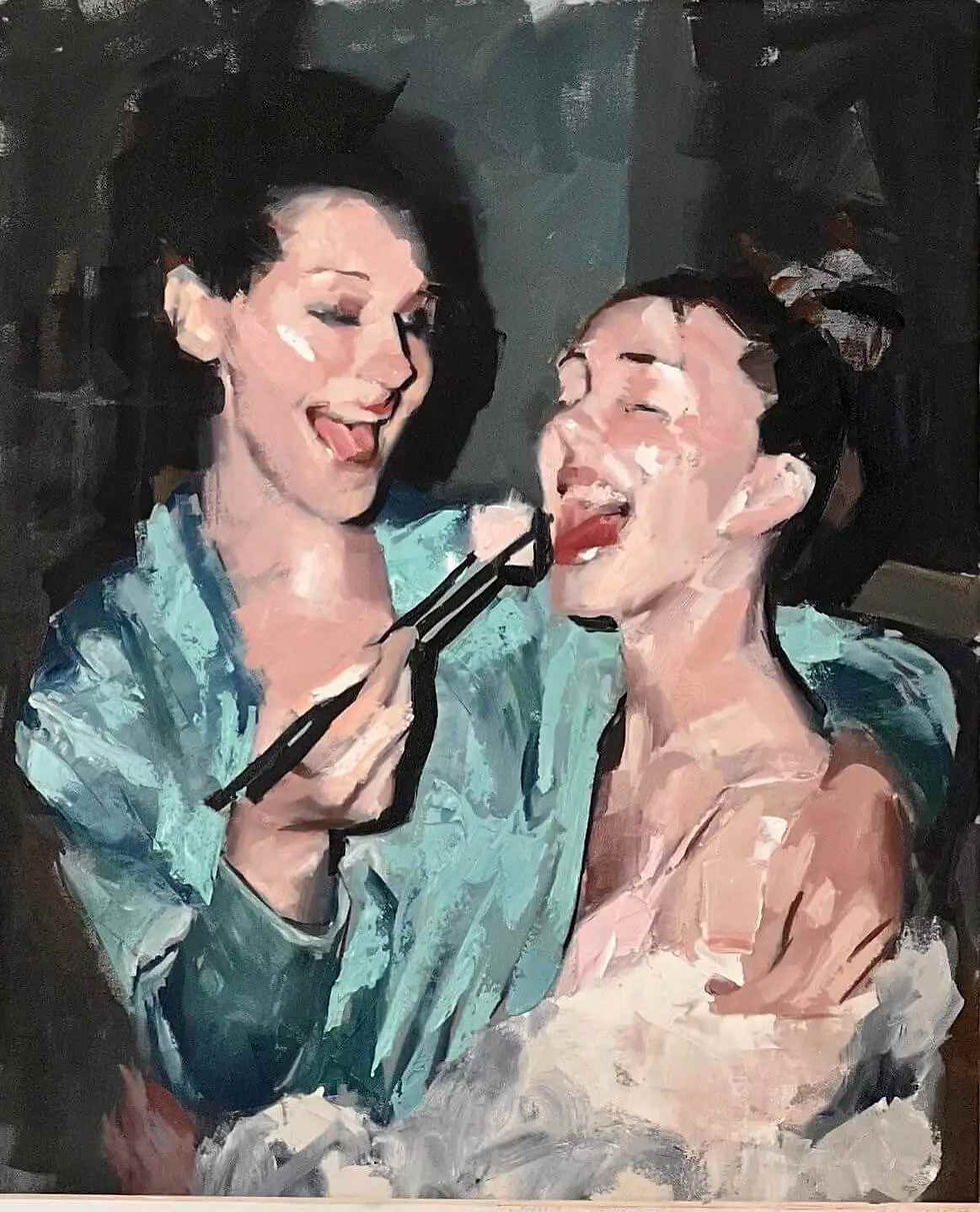Two smiling women in bathrobes, one playfully applying makeup to the other's face with a brush. Background is dark, relaxed atmosphere.