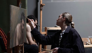 Woman painting from a live model with the man facing down.