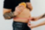 Person measuring waistline while holding a burger — representing losing control of body and weight.