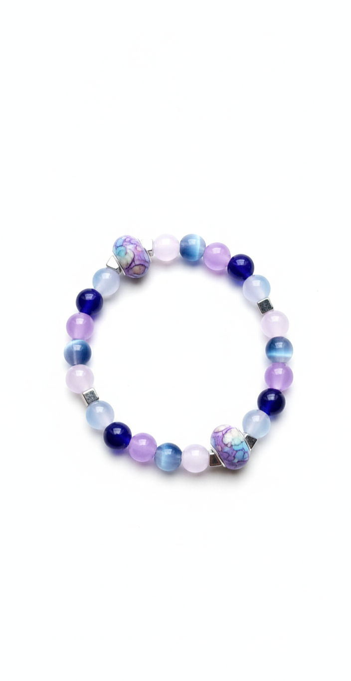 A colorful stretch bracelet featuring various shades of blue and purple round beads, accented with two unique oval-shaped floral patterned beads and small silver spacers, on a white background.