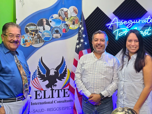Eufracio Gelves poses with cybersecurity experts Stanley Velando and Giselle Oviedo in the Asegúrate Podcast studio at Elite International Consultants. The three are standing and smiling in front of the Elite International Consultants logo, an American flag, and a blue neon "Asegúrate Podcast" sign. The studio features black acoustic panels and a backdrop representing insurance, risk management, and business protection.