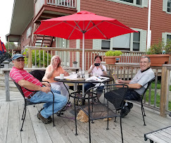 Umbrella, table and chairs situated on a deck outside of Kelly's Landing Restaurant in Greenville, Maine, People eating as they take in the views of Moosehead Lake.