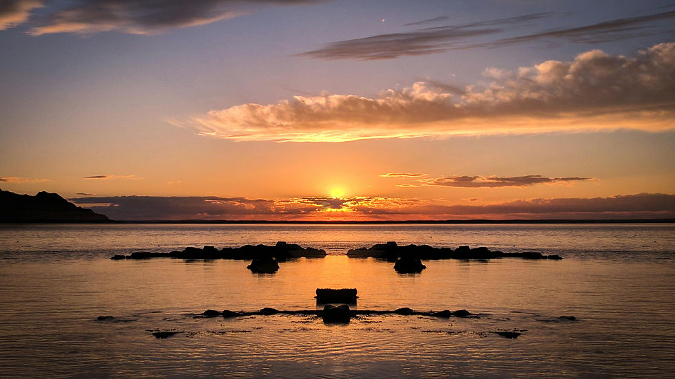 Sunset over calm ocean with rocky silhouettes. Sky painted in orange and purple hues, reflecting on the water. Peaceful and serene mood.