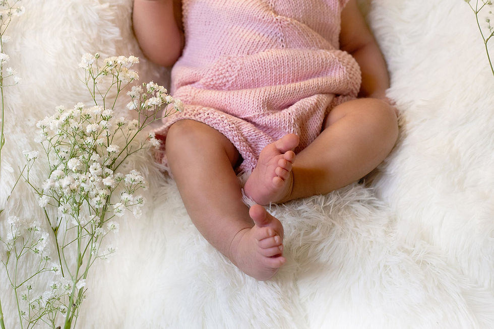 Baby in pink knit outfit on white fur, surrounded by delicate white flowers, creating a soft, serene atmosphere as photographed by Tiffany Edwards, Newborn and Childhood Photographer in Billings Montana